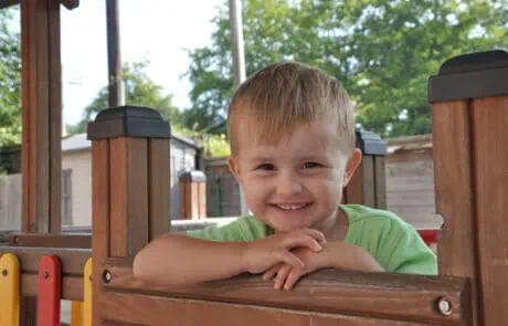 MPHW_Carrers_Image01 Child smiling at camera on wooden play equipment